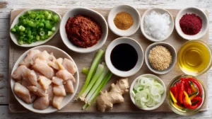 Flat lay of Korean spicy chicken stir-fry ingredients including sliced chicken, gochujang, soy sauce, sesame oil, garlic, ginger, brown sugar, chili flakes, onions, bell peppers, green onions, sesame seeds, and cooking oil arranged on a wooden board.