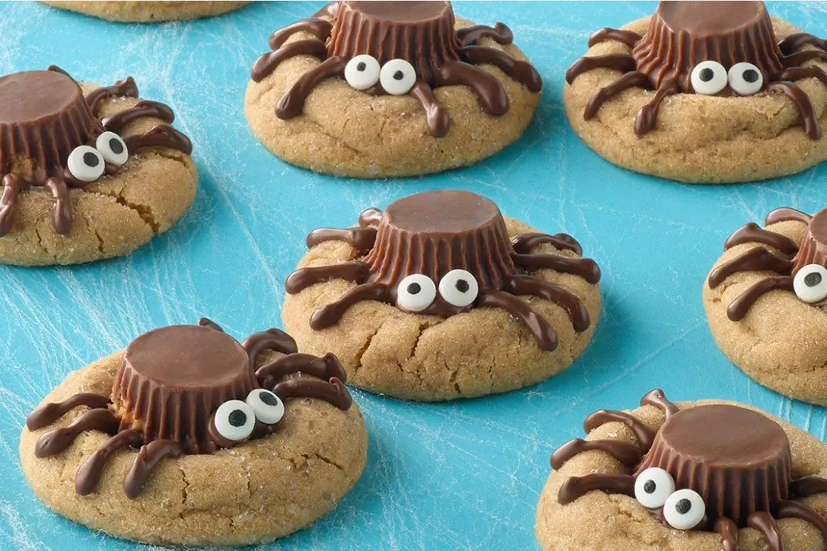 Chocolate spider legs and candy eyes being added to peanut butter cup cookies